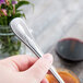 A hand holding a Libbey stainless steel dessert spoon.