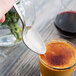 A Libbey stainless steel dessert spoon over a glass of orange liquid.