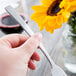 A hand holding a Libbey stainless steel utility/dessert fork with a yellow flower.