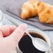 A hand holding a Libbey stainless steel demitasse spoon over a cup of coffee.