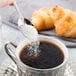 A hand using a Libbey stainless steel demitasse spoon to pour sugar into a cup of coffee.