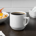 A white Schonwald Continental porcelain mug filled with brown liquid on a table with a bowl of food.