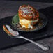 A dessert on a black plate with a World Tableware Resplendence stainless steel dessert spoon.