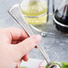 A hand holding a Libbey stainless steel salad fork over a plate of salad.