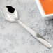 A Libbey stainless steel bouillon spoon next to a bowl of soup.