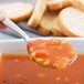 A Libbey stainless steel bouillon spoon holding soup over a bowl of soup.