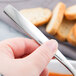 A hand holding a Libbey stainless steel bouillon spoon over a bowl of soup.