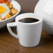 A Schonwald white porcelain espresso cup filled with coffee on a saucer next to a plate of food.