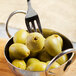 A Master's Gauge stainless steel cocktail fork in a bowl of green olives.