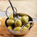 A Master's Gauge stainless steel cocktail fork in a bowl of green olives.