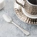 A silver Reserve by Libbey stainless steel demitasse spoon on a white plate with a silver cup and saucer.