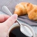 A hand holding a Reserve by Libbey stainless steel demitasse spoon over a cup of coffee.