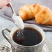 A hand holding a Reserve by Libbey stainless steel demitasse spoon pouring sugar into a cup of coffee.