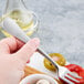 A person's hand holding a Reserve by Libbey stainless steel cocktail fork over a white bowl of food.