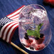 A glass of water with ice, berries, and mint in it.