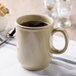 A white Thunder Group Nustone Sand Bulbous Mug on a napkin with a spoon.