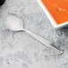 A Libbey stainless steel bouillon spoon next to a bowl of soup.