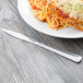 A Libbey stainless steel dinner knife on a table with a plate of food.