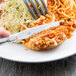 A Libbey stainless steel dinner knife on a plate of food with a fork.