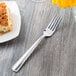 A Libbey stainless steel utility fork on a table next to a plate of food.