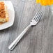 A Libbey stainless steel dinner fork on a table next to a plate of food.