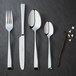 A Chef & Sommelier stainless steel demitasse spoon on a black surface.