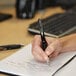 A hand holding a Uni-Ball Signo 207 pen and writing on a notebook.