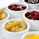 A white tray with small bowls of fruit including cherries in a Hall China bright white fluted ramekin.