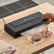 A hand using the Galaxy VME1 vacuum sealer to package meat in a plastic bag.