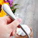 A hand holding a Master's Gauge by World Tableware stainless steel dessert spoon over a cup of whipped cream.