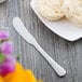 A white plate with butter and a biscuit next to a Reserve by Libbey stainless steel butter spreader.
