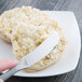 A hand using a Reserve by Libbey stainless steel butter spreader to spread butter on a biscuit.