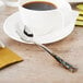 A cup of coffee with a Master's Gauge Pebblestone stainless steel teaspoon on a table.