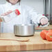 A woman in a white chef's coat pouring milk into a Vollrath sauce pan.