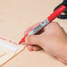 A hand using a Sharpie red fine point permanent marker to write on a piece of paper.