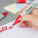 A hand holding a Sharpie red chisel tip permanent marker writing on a piece of paper.