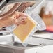 A hand holding a block of cheese in a VacPak-It chamber vacuum packaging pouch.