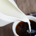 A cup of coffee with milk being poured from a white Villeroy & Boch porcelain creamer.