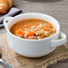 A stackable white porcelain soup cup filled with soup and vegetables.