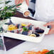 A person pouring oil onto fish wrapped in bacon in a white Villeroy & Boch rectangular baking dish.