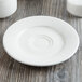 A white Villeroy & Boch porcelain saucer on a wood surface.