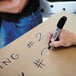 A hand using a Sharpie King Size black chisel tip permanent marker to write on a cardboard box.