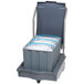 A grey Follett ice cart filled with ice sitting next to a grey ice bin.