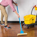 A hand holding an Impact 12 3/4" Sponge Mop with a yellow handle and mopping the floor.