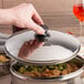 A hand holding a Town stainless steel dim sum steamer cover over a bowl of food.