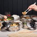 A hand holding chopsticks over a group of Town stainless steel dim sum steamer covers filled with food.