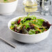 A white porcelain Villeroy & Boch salad bowl filled with lettuce and carrots with a fork and spoon