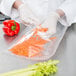 A person in white gloves holding a VacPak-It 10" x 13" vacuum packaging bag of carrots.