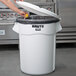 A woman putting food in a white Rubbermaid trash can with a black liner.