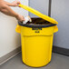 A person putting a bag in a yellow Rubbermaid trash can with a yellow lid.